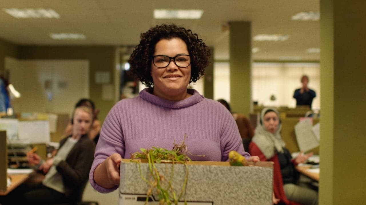 A woman in a purple sweater carries a box of belongings through an office.