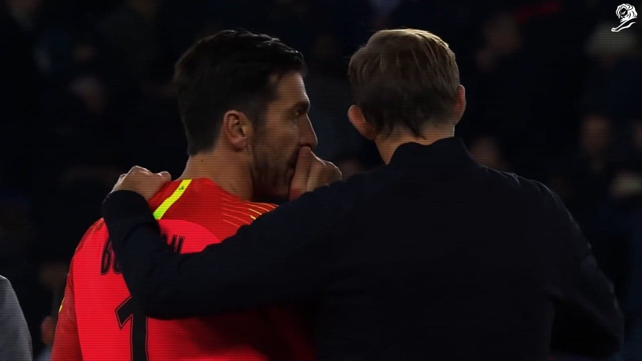 A footballer covers his mouth while speaking to his coach.